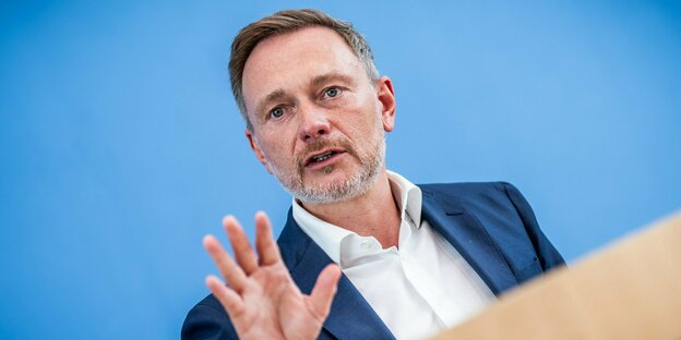 Christian Linnder steht vor einer hellblauen Wand, er trägt ein weisses Hemd mit offenem Kragen, einen Fünf-Tage-Bart und hebt die Hand Christian Linnder steht vor einer hellblauen Wand, er trägt ein weisses Hemd mit offenem Kragen, einen Fünf-Tage-Bart und hebt die Hand