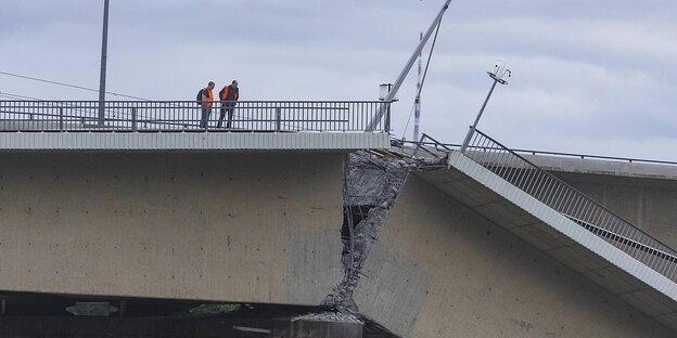 Zwei Männer in Warnwesten stehen auf einer eingestürzten brücke Zwei Männer in Warnwesten stehen auf einer eingestürzten brücke