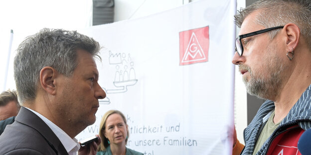 Robert Habeck steht einem Gewerkschafter mit IG-Metall-Jacke gegenüber, dahinter steht eine weitere Person vor einem Banner der Gewerkschaft IG Metall. Robert Habeck steht einem Gewerkschafter mit IG-Metall-Jacke gegenüber, dahinter steht eine weitere Person vor einem Banner der Gewerkschaft IG Metall.