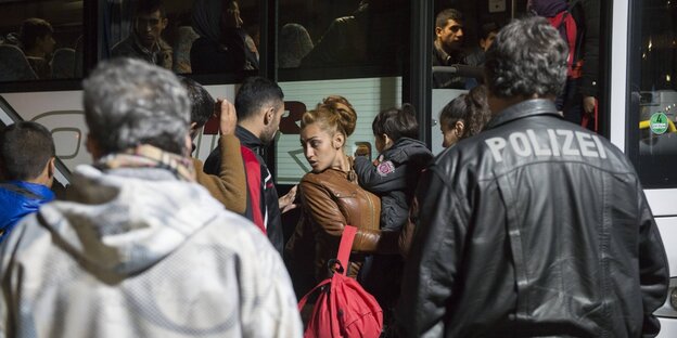 Menschen steigen in einen Bus, in der Bildmitte ist eine Frau, die ein kind auf dem Arm trägt. Sie schaut sich um. Menschen steigen in einen Bus, in der Bildmitte ist eine Frau, die ein kind auf dem Arm trägt. Sie schaut sich um.