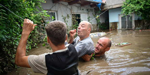 Drei Männer stehen bis zum Kopf im Wasser und halten sich an einer Wäscheleine fest Drei Männer stehen bis zum Kopf im Wasser und halten sich an einer Wäscheleine fest