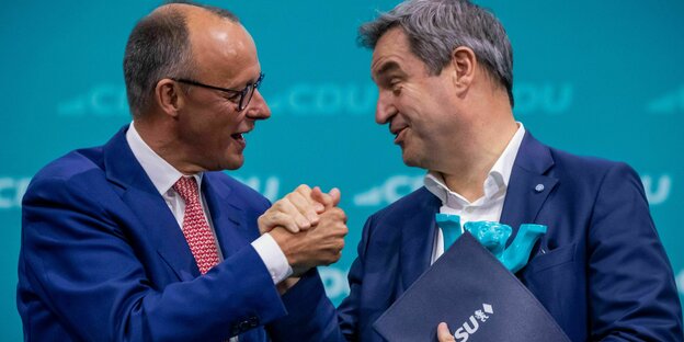 Friedrich Merz und Markus Söder, Schulter an Schulter, halten sich an den Händen und lächeln sich an Friedrich Merz und Markus Söder, Schulter an Schulter, halten sich an den Händen und lächeln sich an