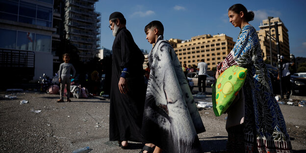 ein Junge in eine Decke ghüllt, ein alter Mann und Mädchen mit Kissen ziehen über eine Straße ein Junge in eine Decke ghüllt, ein alter Mann und Mädchen mit Kissen ziehen über eine Straße