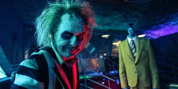 Eine Szene aus dem Film: Beetlejuice schaut in die Kamera, im Hintergrund Bob, ein Zombie im Anzug Eine Szene aus dem Film: Beetlejuice schaut in die Kamera, im Hintergrund Bob, ein Zombie im Anzug