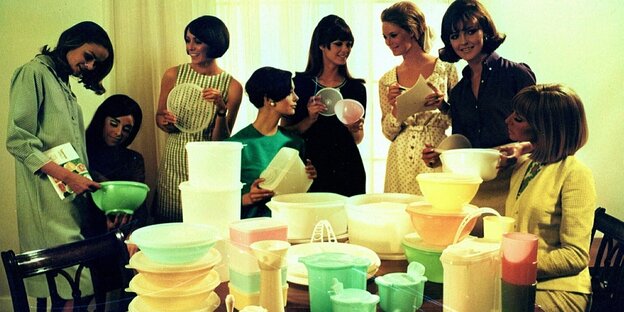 Eine Gruppe von Frauen betrachtet verschiedene Tupperwaren auf einem Tisch. Eine Gruppe von Frauen betrachtet verschiedene Tupperwaren auf einem Tisch.