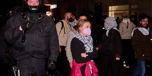 Greta Thunberg steht mit Palästinensertuch neben einem Polizeibeamten in einer protestierenden Menge Greta Thunberg steht mit Palästinensertuch neben einem Polizeibeamten in einer protestierenden Menge