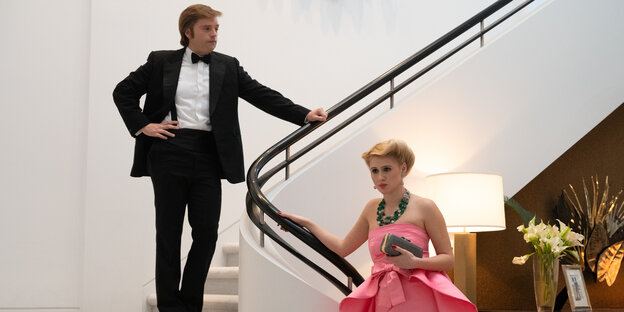 Ein mann in scharzem Anzug steht auf einer Treppe, eine Frau im rosa Abendkleid hält sich am Treppengelände fest Ein mann in scharzem Anzug steht auf einer Treppe, eine Frau im rosa Abendkleid hält sich am Treppengelände fest