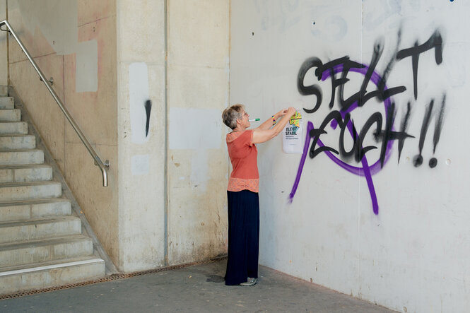 Eine Person klebt ein Plakat an eine Betonwand