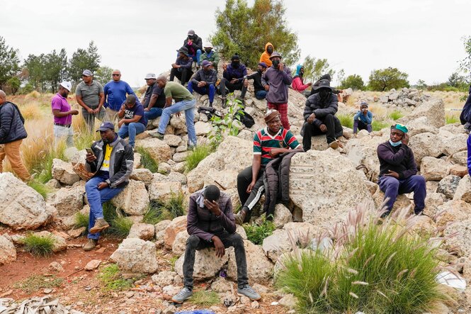 Mehrere Personen sitzen niedergeschlagen auf Felsen.