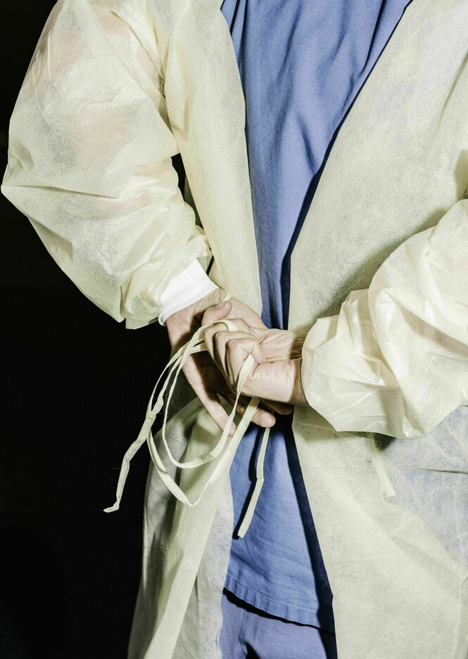 Eine Person zieht sich einen Schutzkittel an