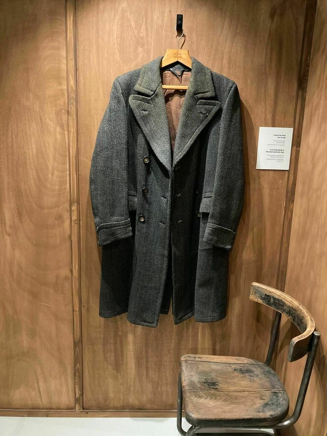 Ein alter Mantel hängt an einem Haken an der Holzwand