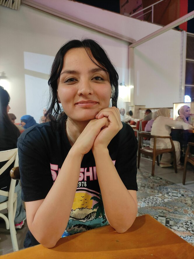 Sally Moon sitzt lächelnd an einem Tisch - sie hat halblange dunkle Haare