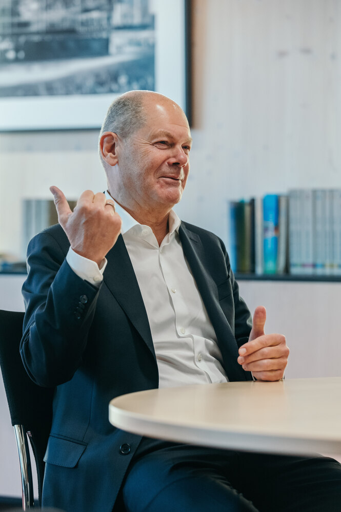 ein Mann im Anzug sitzt an einem Tisch und gestikuliert